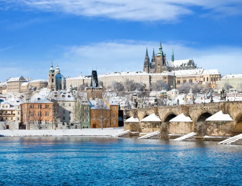 pacote leste europeu 2027 - Praga no inverno: a histórica Ponte Carlos e o Castelo de Praga formam uma das paisagens mais encantadoras da República Tcheca, com telhados cobertos de neve às margens do Rio Vltava.