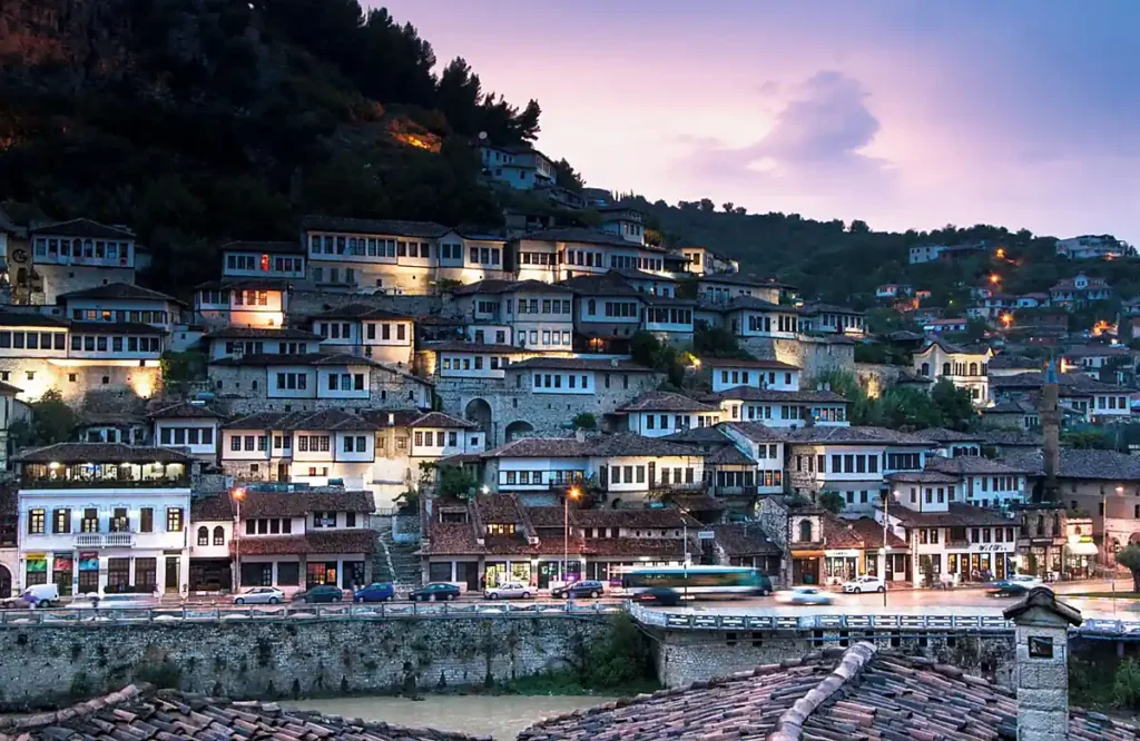 Berat, conhecida como a Cidade das Mil Janelas, é um dos destinos históricos mais famosos da Albânia e Patrimônio Mundial da UNESCO. A fotografia destaca as tradicionais casas otomanas de fachadas brancas, grandes janelas e telhados de terracota que caracterizam os bairros históricos da cidade. Localizada no centro-sul da Albânia, Berat preserva um importante conjunto arquitetônico dos períodos otomano e medieval, sendo uma das cidades mais fotogênicas dos Bálcãs.