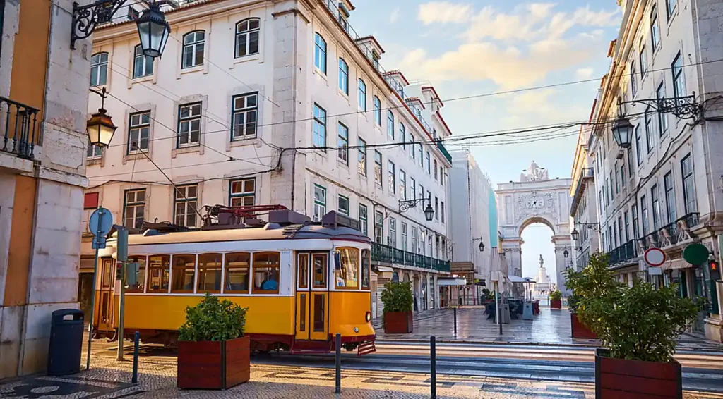 Os elétricos amarelos são um dos símbolos mais conhecidos de Lisboa. A fotografia mostra o transporte histórico circulando pela região da Baixa Pombalina, próximo ao Arco da Rua Augusta, importante monumento do centro da capital portuguesa.