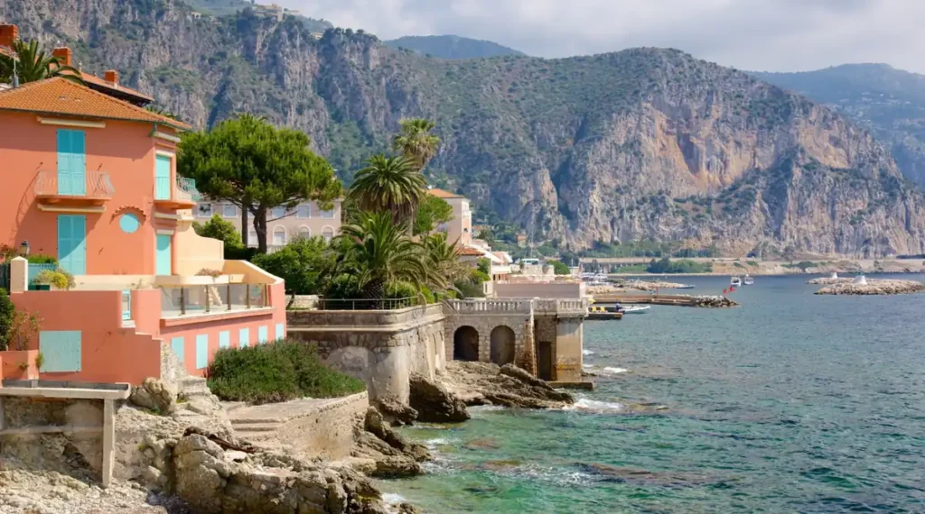 Arquitetura mediterrânea e paisagem costeira da Côte d’Azur, no sul da França, com casas em tons pastel, palmeiras e construções históricas próximas ao mar. A Riviera Francesa é famosa por suas vilas à beira-mar, enseadas de águas cristalinas, montanhas próximas ao litoral e paisagens que combinam natureza e elegância mediterrânea.
