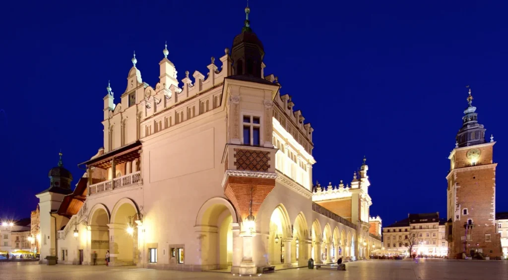 Mercado de Tecidos de Cracóvia, ou Sukiennice, iluminado à noite na Praça do Mercado. O edifício histórico é um dos símbolos da cidade e abriga lojas de artesanato e lembranças, enquanto a Torre da Prefeitura completa a paisagem arquitetônica de uma das praças medievais mais famosas da Europa.