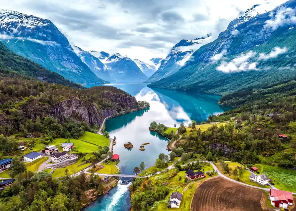 Paisagem espetacular dos fiordes noruegueses, com águas cristalinas, montanhas cobertas de neve e vilarejos cercados pela natureza. Os vales glaciais da Noruega oferecem algumas das vistas panorâmicas mais impressionantes da Escandinávia, combinando montanhas, lagos e vegetação exuberante.