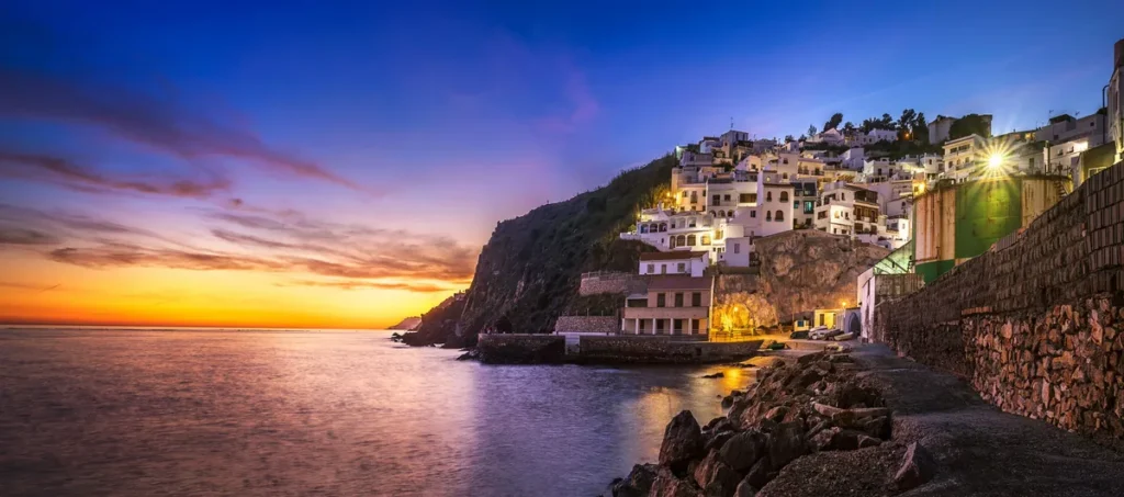 Pôr do sol na costa da Andaluzia, no sul da Espanha, com casas brancas construídas sobre uma encosta à beira-mar. A paisagem combina arquitetura mediterrânea, falésias e as cores intensas do entardecer.