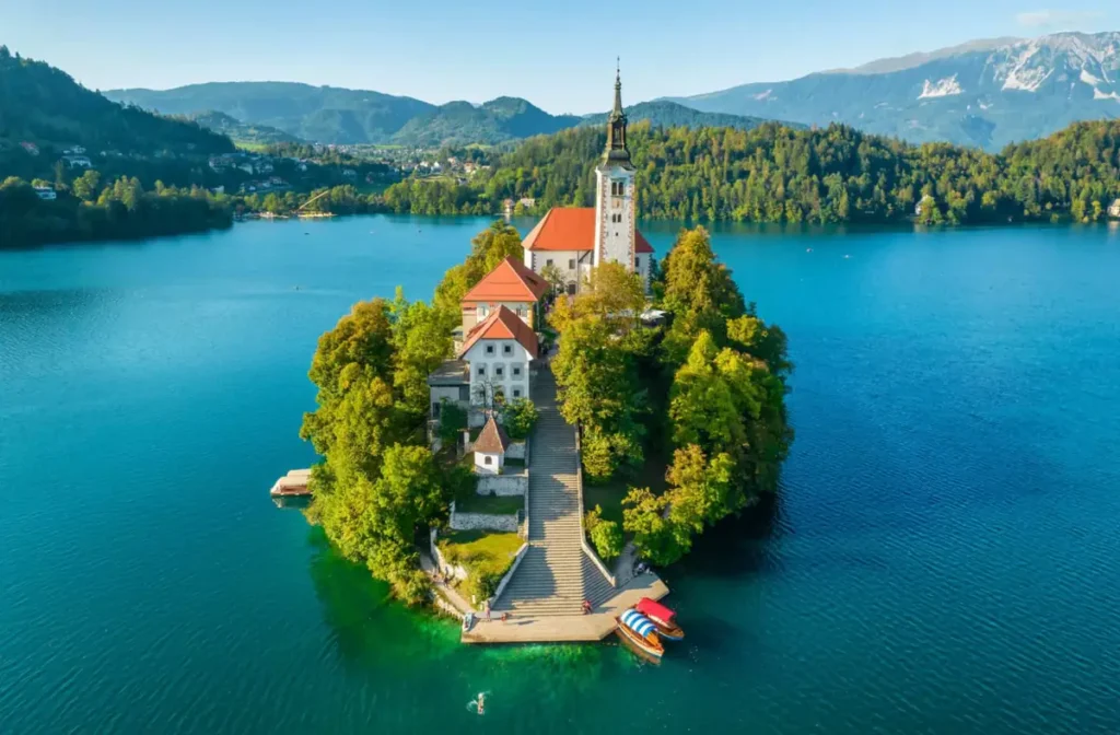 Ilha do Lago Bled vista de cima, com a Igreja da Assunção de Maria e sua famosa escadaria de pedra. Cercada pelas águas azul-turquesa do lago e pela vegetação dos Alpes Julianos, a ilha é uma das atrações turísticas mais emblemáticas da Eslovênia.
