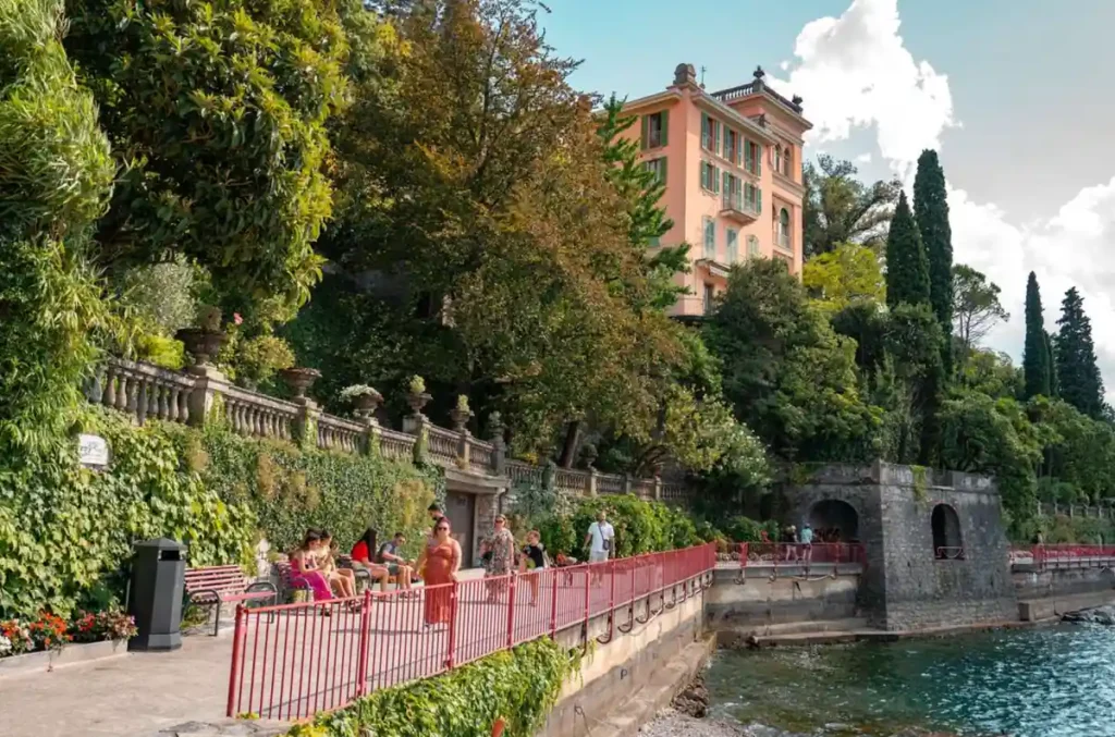 Passeio à beira do Lago di Como, no norte da Itália, cercado por jardins mediterrâneos, árvores e elegantes construções históricas. A paisagem revela a atmosfera sofisticada dos vilarejos às margens do lago, um dos destinos mais famosos da região da Lombardia.