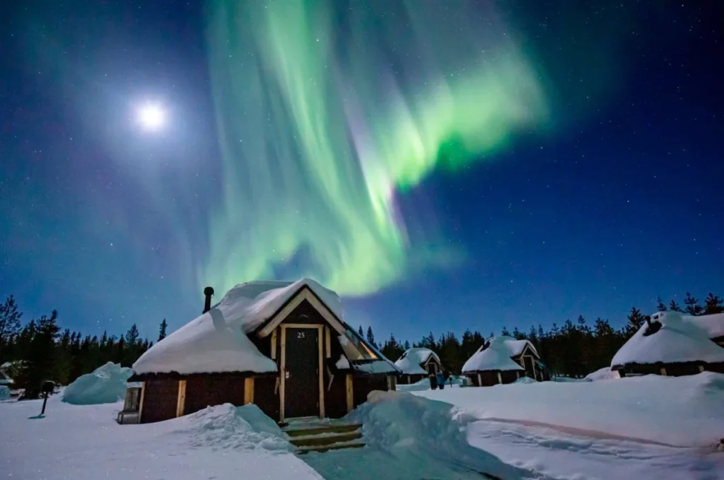 Aurora boreal na Lapônia, um dos fenômenos naturais mais impressionantes do norte da Europa. Durante as noites de inverno, cortinas de luz verde podem iluminar o céu acima de cabanas e florestas nevadas, proporcionando uma experiência inesquecível para viajantes que desejam observar a aurora boreal.