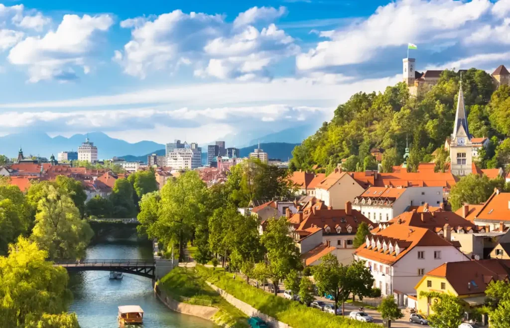 Vista panorâmica de Ljubljana, destacando o rio Ljubljanica e o Castelo de Ljubljana, situado no alto de uma colina. A capital eslovena combina arquitetura histórica, áreas verdes e paisagens montanhosas, oferecendo um cenário característico da Europa Central.