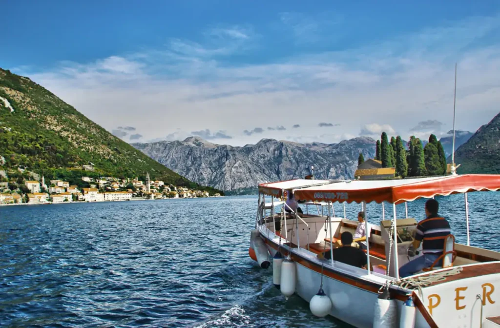 Barco turístico navegando pela Baía de Kotor, em Montenegro, com a vila histórica de Perast e montanhas ao fundo.