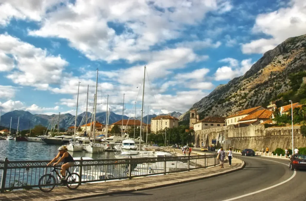 Marina de Kotor, em Montenegro, com veleiros ancorados, muralhas históricas, montanhas e passeio à beira-mar.