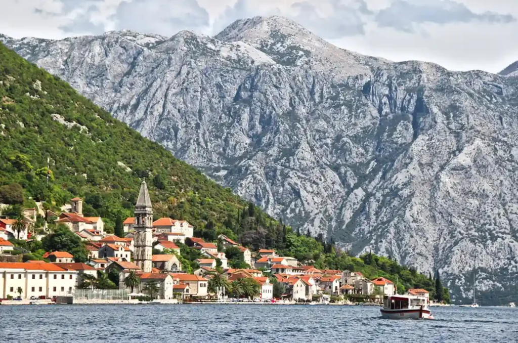 Vila histórica de Perast, em Montenegro, com casas de telhados vermelhos, campanário de pedra e montanhas imponentes na Baía de Kotor.