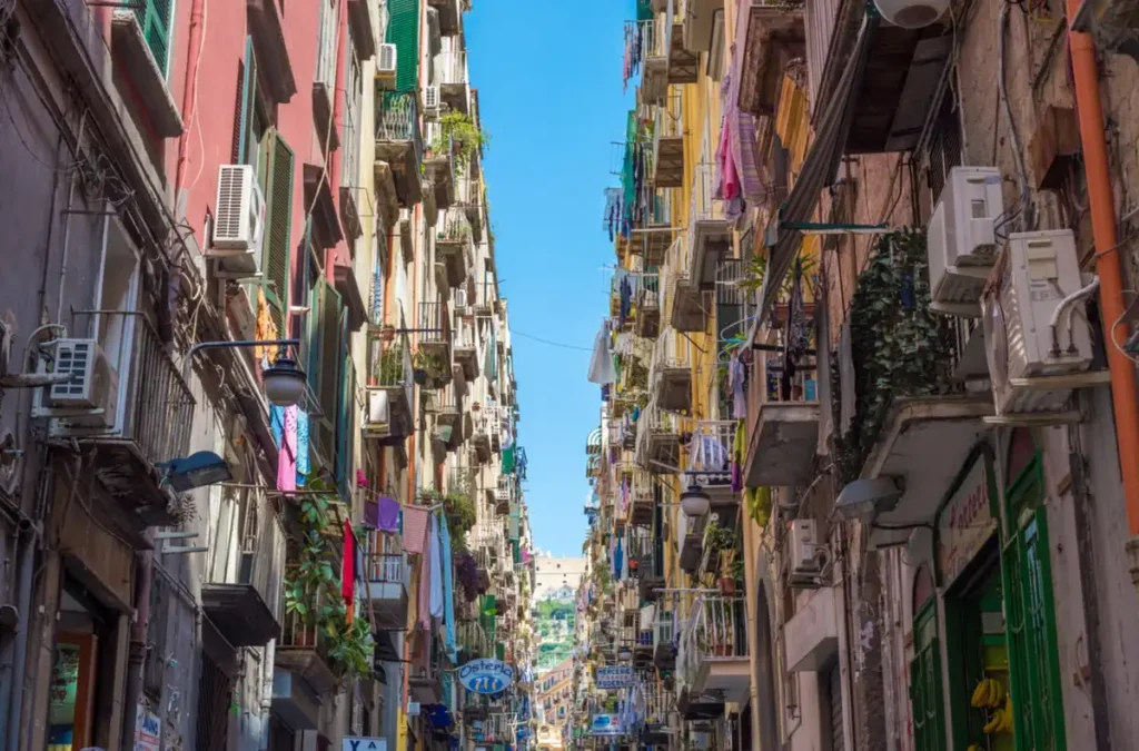 Centro histórico de Nápoles, no sul da Itália, com suas ruas estreitas, edifícios antigos, varandas e roupas estendidas nas janelas. A arquitetura e o cotidiano dos bairros tradicionais revelam a atmosfera autêntica da cidade, conhecida por sua cultura, gastronomia e patrimônio histórico reconhecido pela UNESCO.