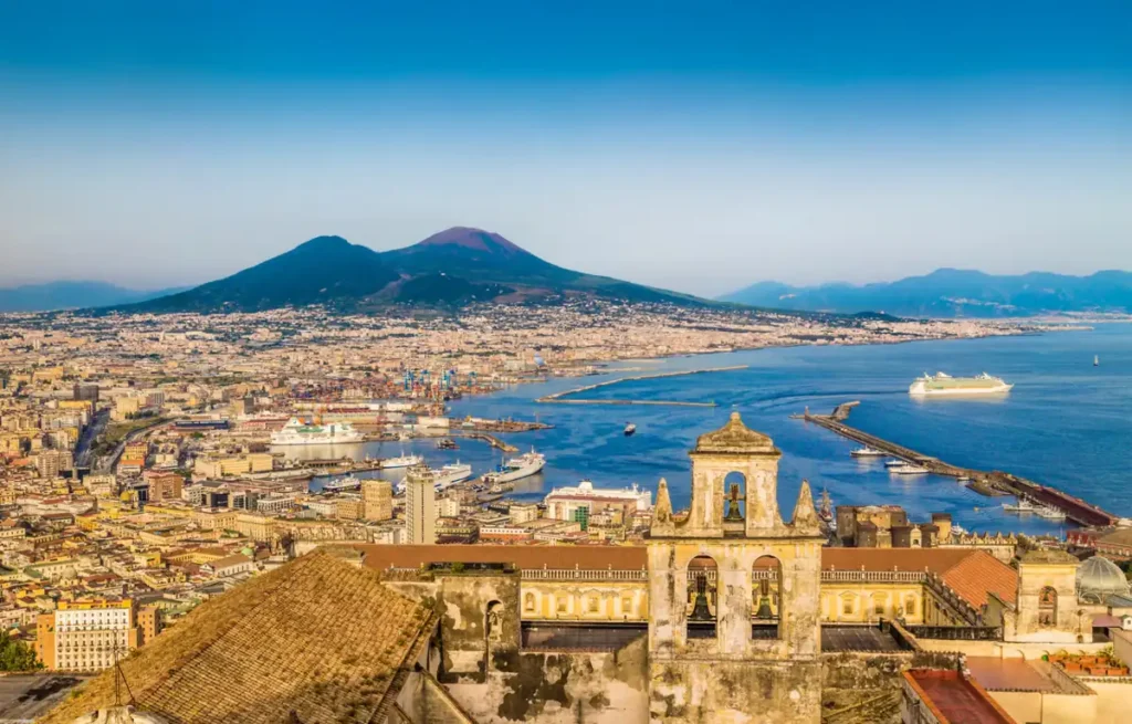 Vista panorâmica de Nápoles e do Monte Vesúvio, um dos vulcões mais famosos da Itália, com o Golfo de Nápoles e seu movimentado porto. A paisagem reúne o centro urbano, o Mar Tirreno e o vulcão responsável pela erupção que destruiu Pompeia em 79 d.C., um dos acontecimentos mais conhecidos da história romana.