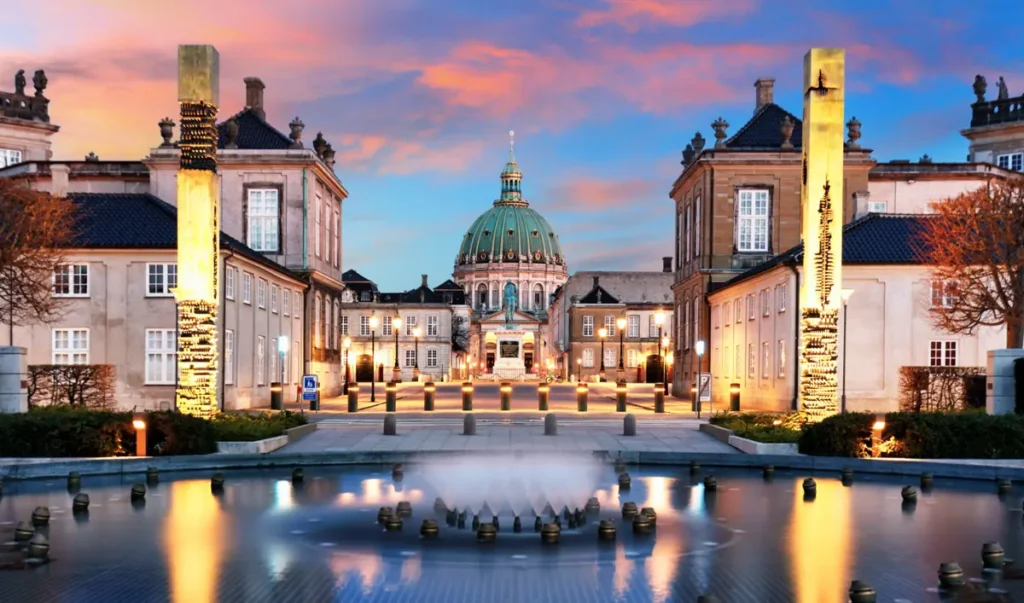 Palácio de Amalienborg, residência oficial da família real dinamarquesa, em Copenhague, capital da Dinamarca. A fotografia destaca a arquitetura monumental do complexo, a cúpula da Igreja de Mármore (Frederik's Church) e a iluminação do entardecer. Amalienborg é uma das principais atrações históricas e arquitetônicas da cidade.
