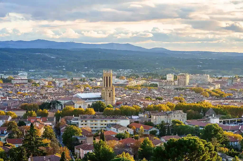 Panorama de Aix-en-Provence, cidade histórica da região Provence-Alpes-Côte d'Azur, no sul da França. A paisagem destaca os telhados tradicionais, a torre da Catedral Saint-Sauveur, a arquitetura provençal e as áreas arborizadas que cercam a cidade. Conhecida por suas fontes, mercados e patrimônio cultural, Aix-en-Provence é um dos destinos mais representativos da Provença.