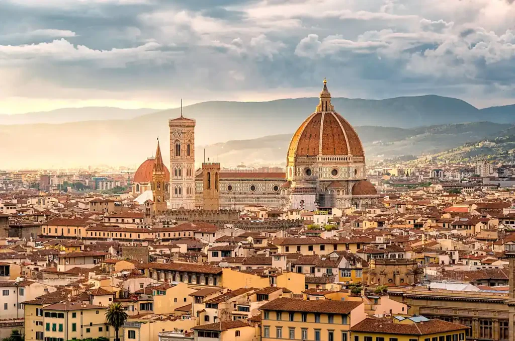 O panorama de Florença revela a famosa cúpula do Duomo, projetada por Filippo Brunelleschi, cercada por edifícios históricos e telhados de terracota. A paisagem representa o patrimônio arquitetônico da capital da Toscana, considerada um dos principais berços do Renascimento italiano.