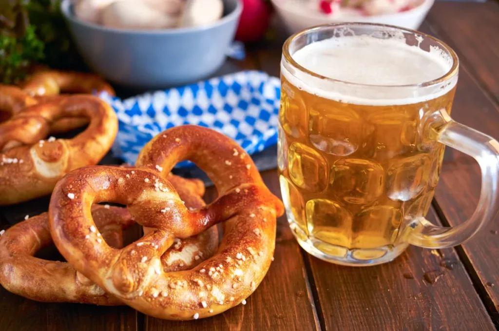 Pretzels tradicionais acompanhados de uma caneca de cerveja clara, uma combinação bastante popular na gastronomia da Áustria e da região alpina de língua alemã. Conhecido localmente como Brezel, o pão apresenta formato entrelaçado, casca dourada, textura macia por dentro e pequenos cristais de sal grosso na superfície. Frequentemente servido em cervejarias, restaurantes e mercados tradicionais, é um dos acompanhamentos mais característicos da cultura gastronômica da região. Em Salzburgo, os visitantes encontram diferentes variedades de pretzels em padarias, cafés e estabelecimentos típicos, especialmente nas áreas turísticas do centro histórico. A combinação de pães artesanais e cervejas regionais faz parte das experiências culinárias procuradas por quem visita a Áustria.