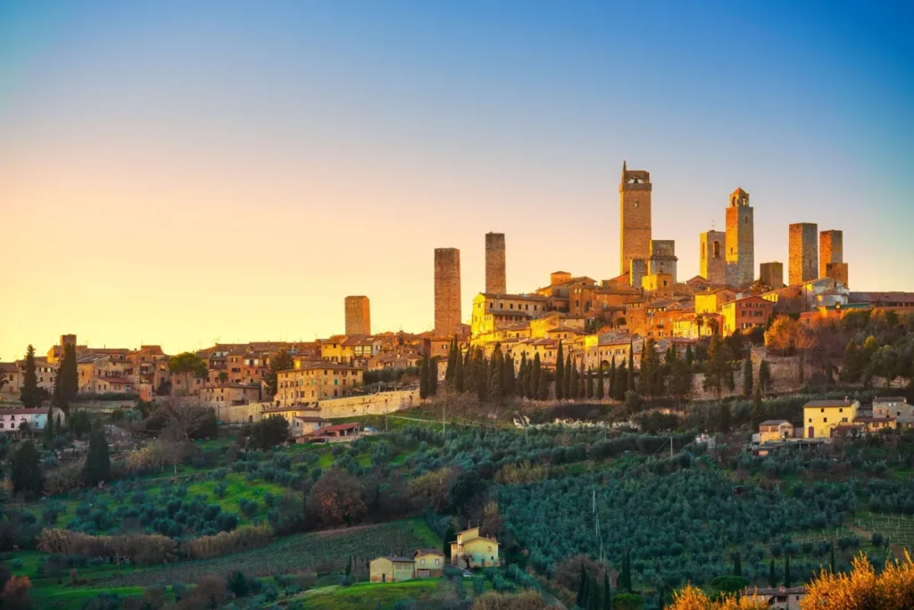 San Gimignano ao entardecer, com suas famosas torres medievais destacadas pela luz dourada sobre as colinas da Toscana.