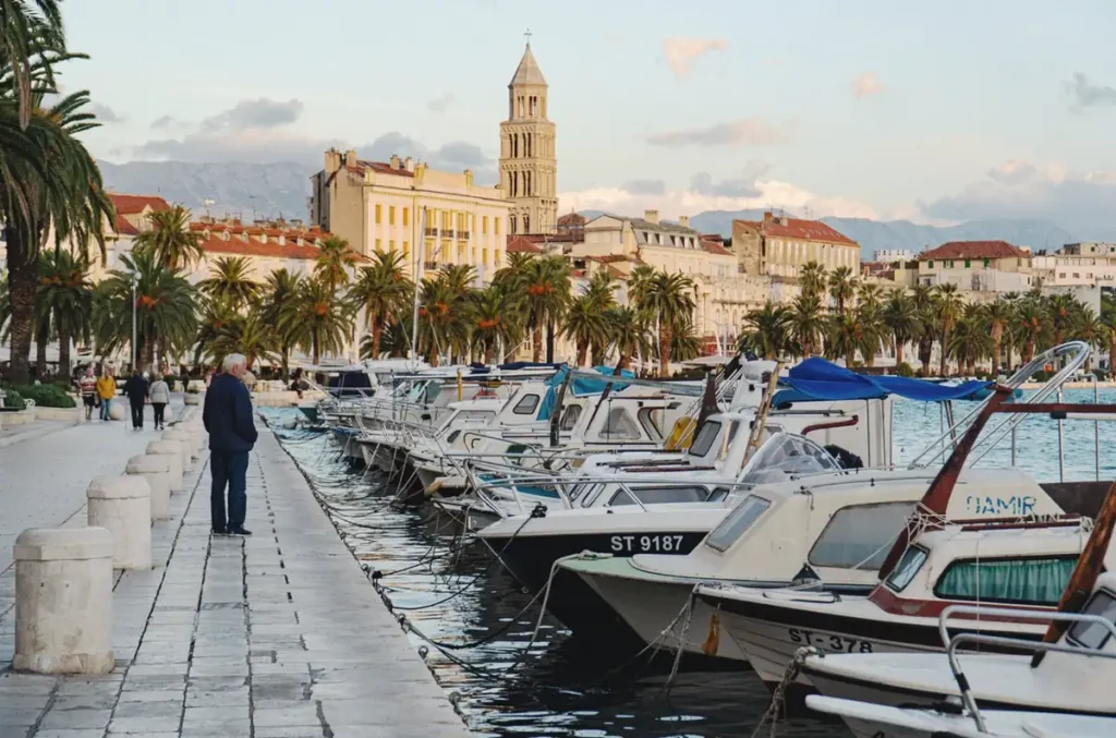 Riva de Split, famoso calçadão à beira-mar da cidade croata, com palmeiras, barcos e edifícios históricos. Localizada junto ao centro antigo e ao Palácio de Diocleciano, a promenade é um dos principais pontos de encontro e passeios turísticos de Split, às margens do Mar Adriático.