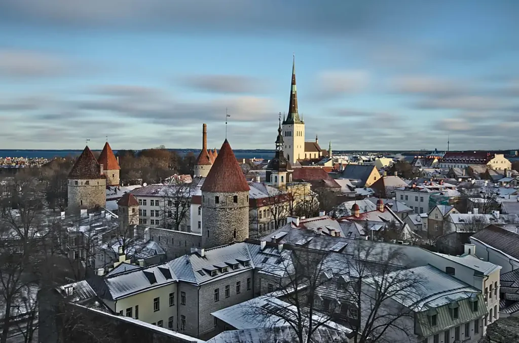 Centro histórico de Tallinn, capital da Estônia, durante o inverno. As torres das antigas muralhas, os telhados nevados e a Igreja de São Olavo revelam a arquitetura medieval preservada da cidade, reconhecida como Patrimônio Mundial da UNESCO.