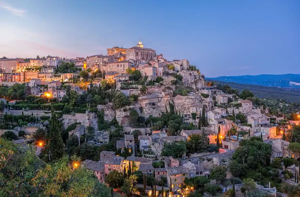 Gordes, uma das vilas mais famosas da Provence, localizada na região do Luberon, no sul da França. Construída sobre uma colina, a vila medieval é conhecida pelas casas de pedra, ruas estreitas, arquitetura provençal e vistas panorâmicas. Ao entardecer, a iluminação das construções históricas cria uma das paisagens mais características do interior da Provença.