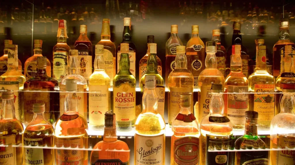 Exposição de uma coleção de garrafas de whisky escocês, uma das bebidas mais tradicionais e reconhecidas da Escócia. A fotografia apresenta diferentes marcas e estilos de Scotch whisky, organizados em uma vitrine de vidro iluminada, com rótulos históricos, embalagens variadas e bebidas em tonalidades que vão do dourado-claro ao âmbar intenso. O whisky é parte importante da identidade cultural escocesa, e Edimburgo oferece diversas experiências turísticas relacionadas à bebida, incluindo degustações, exposições e visitas a estabelecimentos especializados. A imagem representa a tradição da produção de whisky na Escócia e sua relevância para o turismo gastronômico e cultural do país.